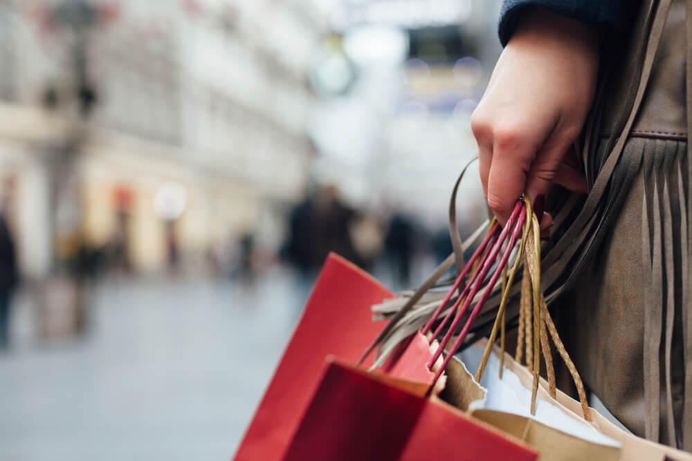 consumidora andando em local publico com sacolas de compras em maos