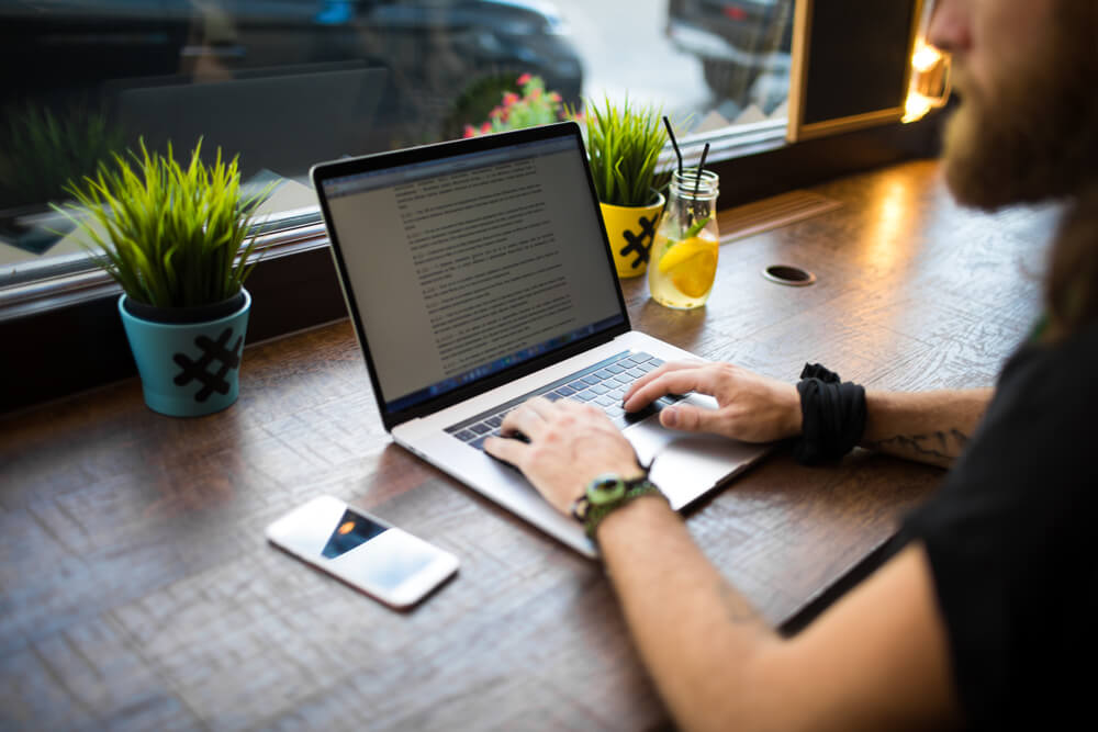 homem escrevendo redaçao publicitaria em laptop sob mesa com decoraçoes